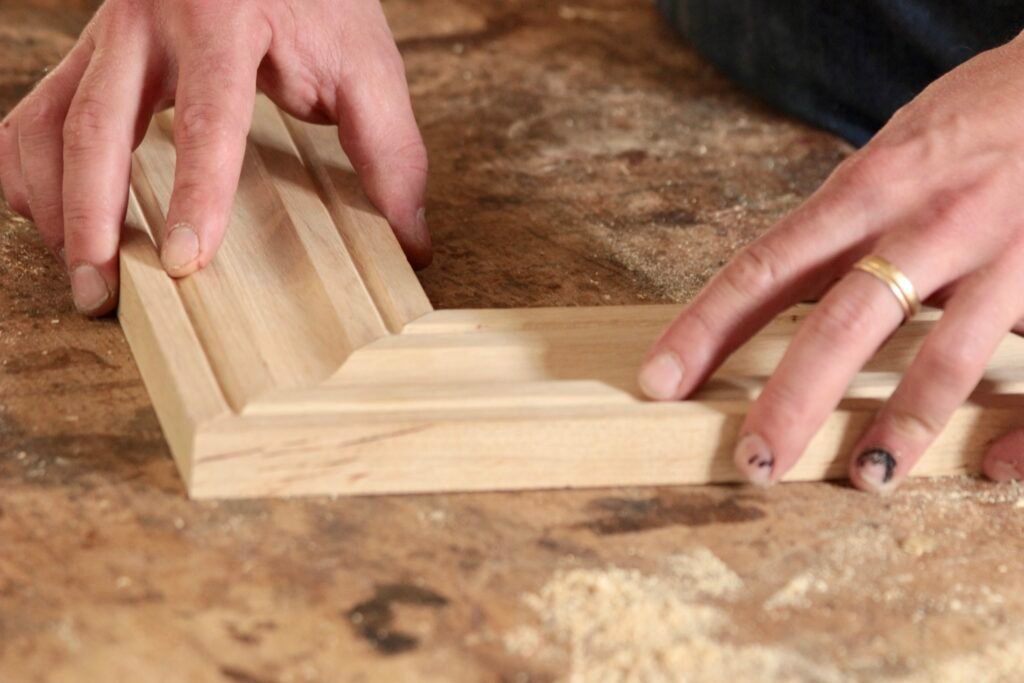 Mains d’artisan ajustant un angle de cadre pour encadrement en bois sur un établi